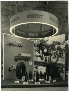 Veduta frontale dello stand Pirelli. Esposizione della gamma di pneumatici Pirelli. Alle pareti pannelli fotografici illustrativi.