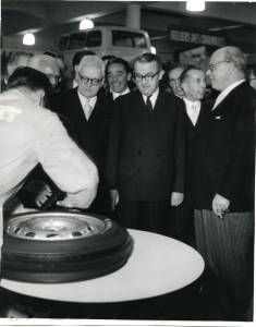 The President of the Swiss Confederation, Max Petitpierre, observes one of the phases of assembly of the BS3 tyre at the Pirelli stand. To his right, Mr. Albert Nussbaumer, President of the Societè Internationale Pirelli of Basel. In the background are other notable government officials.