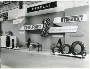Veduta esterna dello stand Pirelli allestito al XXXI Salone Internazionale delle macchine agricole del 1960. In particolare si riconosce un pannello pubblicitario per il pneumatico Cinturato e una selezione di pneumatici Pirelli per agricoltura in esposizione.