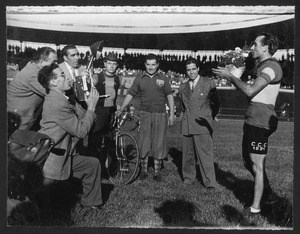 Il vincitore Alfo Ferrari insieme ad altre persone, tra cui altri corridori e un fotografo: è riconoscibile l'ex corridore Gaetano Belloni, campione del ciclismo negli anni Dieci e Venti