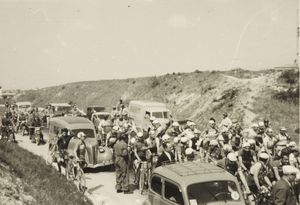 Il gruppo di corridori in una strada, con alcuni furgoncini, alla partenza