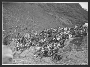 Alcuni spettatori seduti su rocce sul fianco di un monte