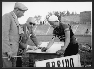 L'arrivo del vincitore della corsa eliminatoria veneta, Arturo Ferrari: il corridore sta firmando, all'interno di un campo sportivo, il foglio di arrivo, appoggiato su un banco