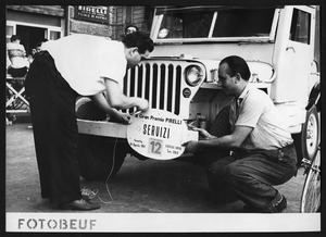 Due uomini applicano una targa a un'auto del Servizio Corse