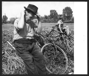 Un uomo anziano e un bambino seduti su un covone di fieno, al quale è appoggiata una bicicletta