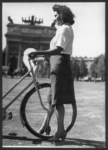 Una giovane con una bicicletta: sullo sfondo è visibile l'Arco della Pace