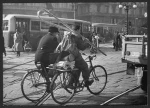 Il passaggio di due uomini in bicicletta: uno di loro sta trasportando materiali per il lavoro