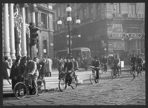 Il passaggio di alcune persone in bicicletta in piazza Cordusio a Milano: sulla sinistra è visibile il Palazzo del Credito Italiano, sulla destra Palazzo Biandrà