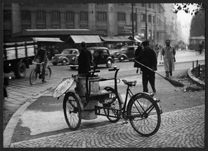 Un furgoncino a pedali attrezzato per la pulizia delle strade in piazzale Loreto: sullo sfondo è visibile il palazzo all'angolo tra piazzale Loreto e viale Abruzzi che ospita tra il 1945 e il 1960 la sede centrale della Pirelli
