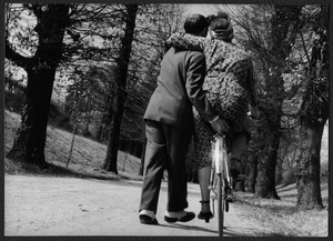 Un sentiero in un parco: un uomo insegna a una donna ad andare in bicicletta