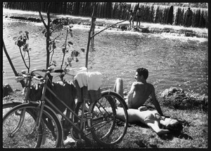 Alcuni giovani vicino a uno specchio d'acqua: le biciclette sono appoggiate a un arbusto