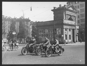 Tre persone in motocicletta a Milano, in piazzale Principessa Clotilde: sullo sfondo, Porta Nuova con i caselli daziari, edificata su progetto dell'architetto Giuseppe Zanoia