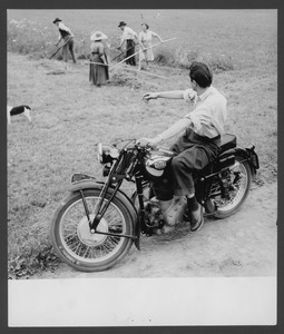 Un uomo in sella a una motocicletta Gilera Saturno Sport: sullo sfondo, persone al lavoro in un campo