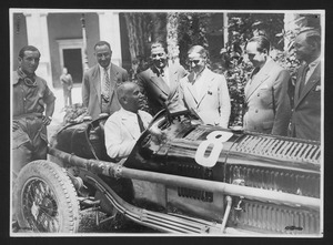 Benito Mussolini su Alfa Romeo insieme ad altre persone, tra le quali sono riconoscibili Tazio Nuvolari e il direttore generale dell'Alfa Romeo Prospero Gianferrari (entrambi al centro). L'automobile è probabilmente l'Alfa Romeo P3 con cui Nuvolari vinse la Coppa Acerbo disputatasi il 14 agosto 1932