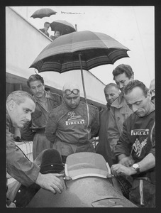 Il pilota Juan Manuel Fangio e l'attore Amedeo Nazzari osservano i meccanici al lavoro: l'immagine è stata pubblicata da Fatti e Notizie (anno II, n. 5, maggio 1951, p. 2)