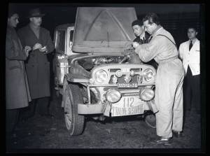 Un meccanico versa del liquido nel vano motore della Fiat Campagnola targata 127012.TO durante il III Rally del Sestriere del 22-25 febbraio 1952. Tre uomini lo osservano.